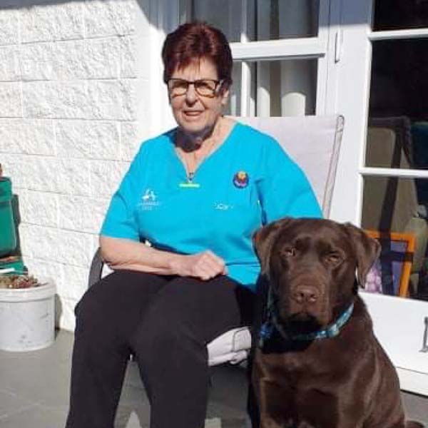 Veterinary Nurse Marilyn sitting outdoors in her Avonhead Vets scrubs with her chocolate Labrador Retriever, Jed.
