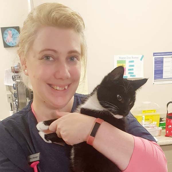 Veterinary Nurse Ashley smiling while holding a black and white domestic short-haired cat at Avonhead Vets.