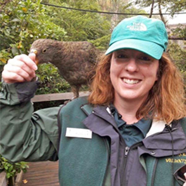 Veterinary Nurse Averlea smiling with a native New Zealand kea perched on her shoulder, eating food from her hand.
