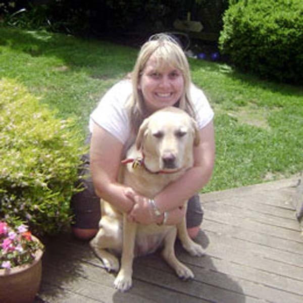 Veterinary Nurse Olivia hugging Bella, her yellow Labrador Retriever, on a wooden deck in her backyard.