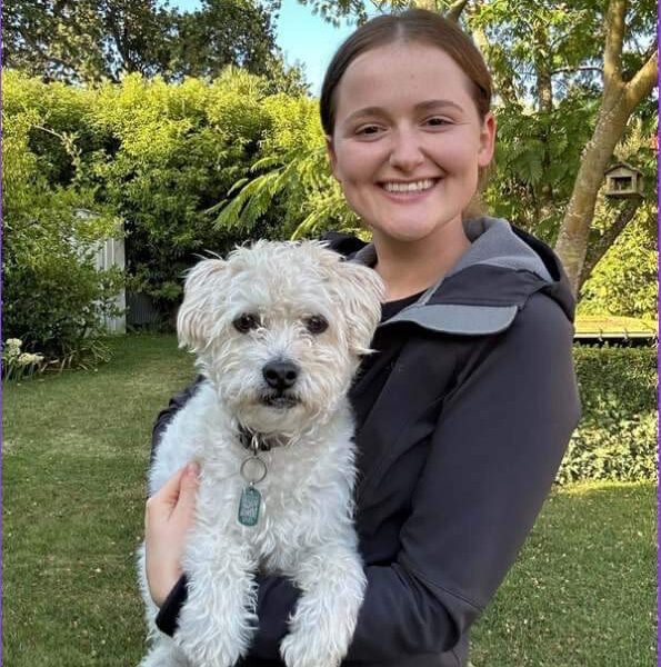 Veterinarian Dr Grace Mathews holding her family’s white Maltese in a lush green garden.